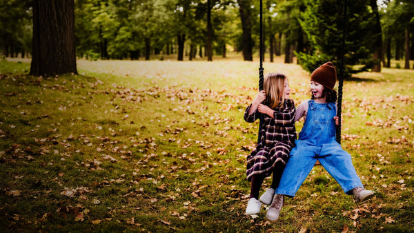 Two children sitting on a swing in a park with fallen leaves on the ground